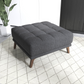 Modern dark gray upholstered ottoman with wooden legs on a patterned rug in a stylish living room