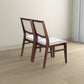 Pair of modern wooden dining chairs with beige upholstery on light wood floor
