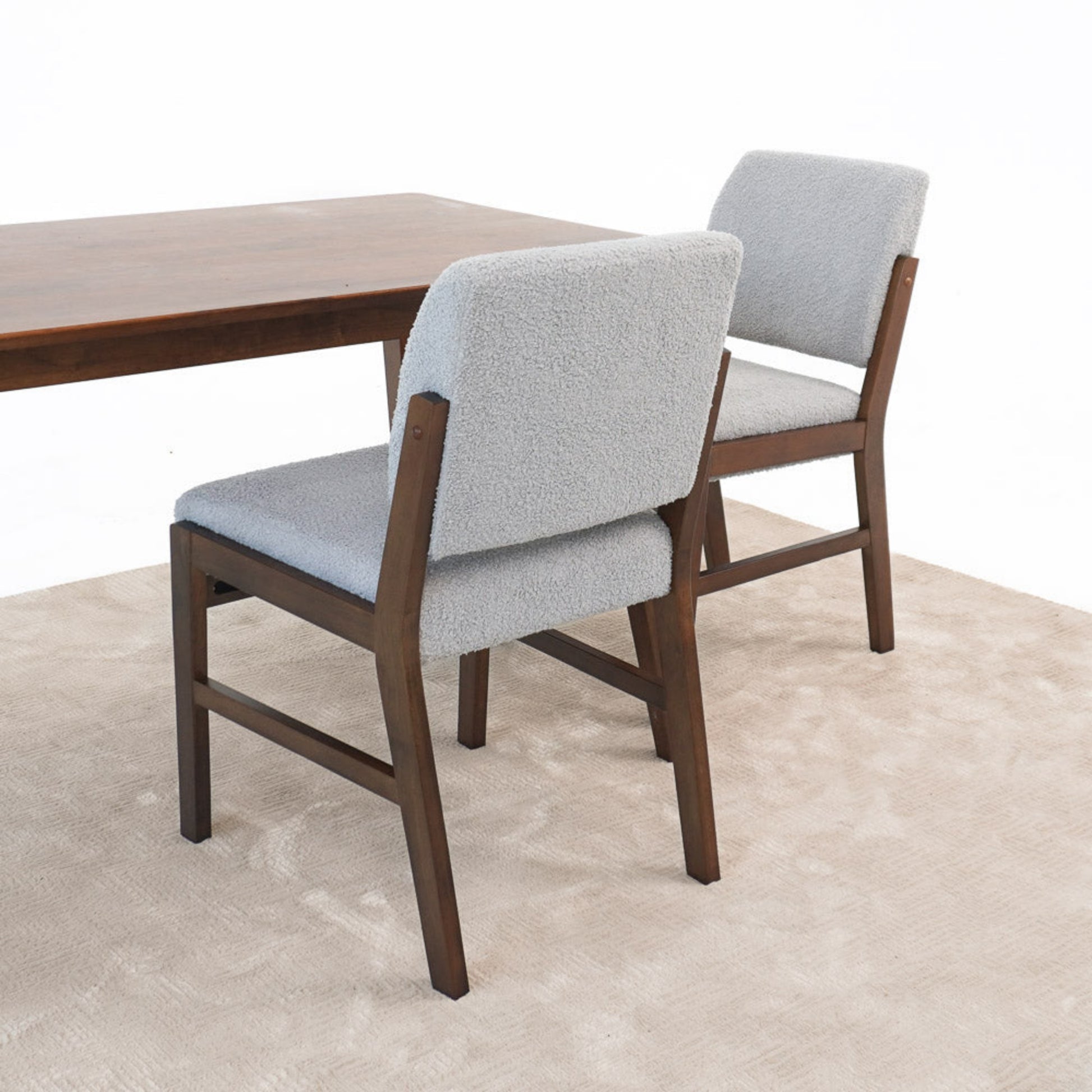 Modern dining room chairs with light gray upholstery and wooden frames next to a wood table