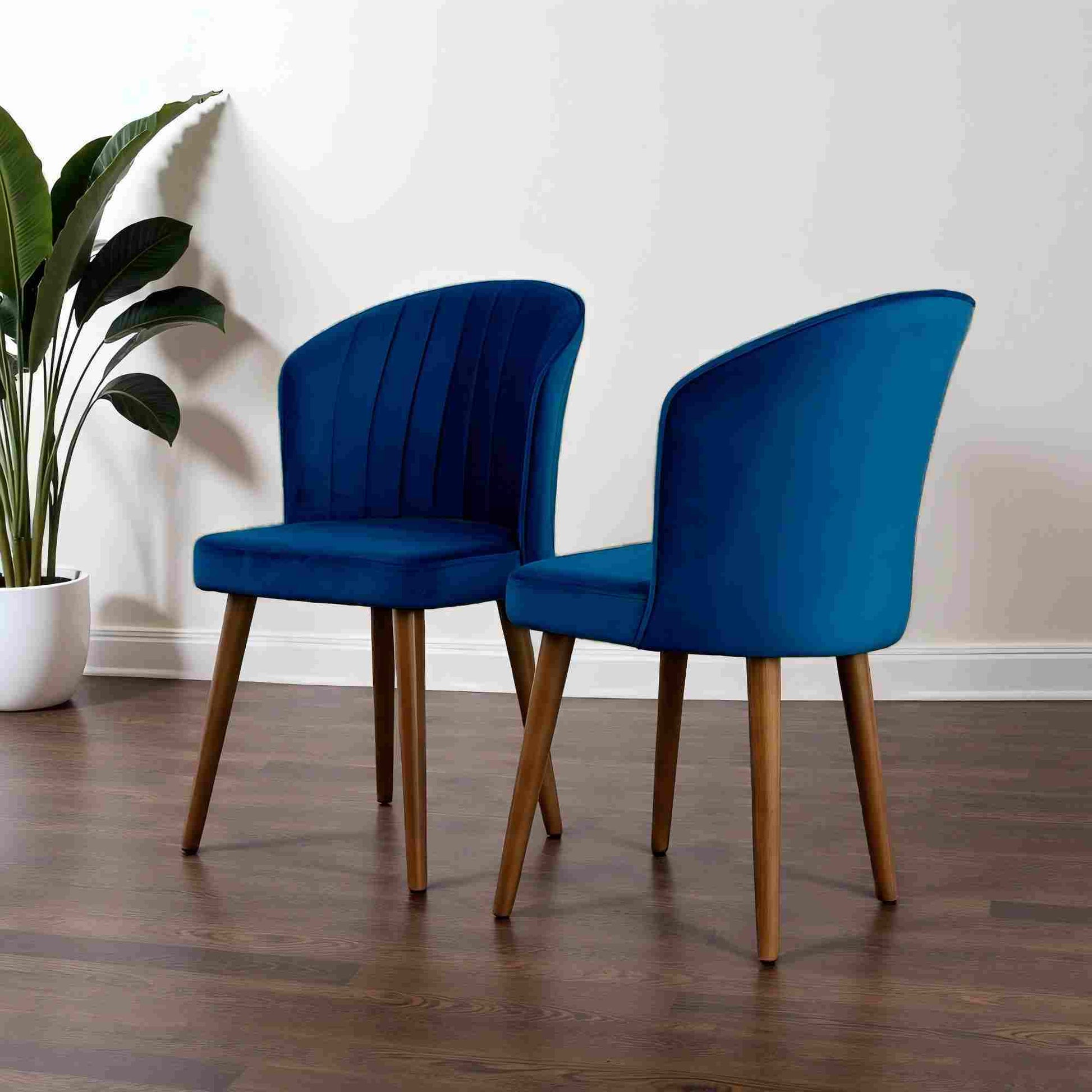 Two modern blue velvet dining chairs with wooden legs on hardwood floor, FredCo International furniture