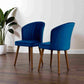 Two modern blue velvet dining chairs with wooden legs on hardwood floor, FredCo International furniture