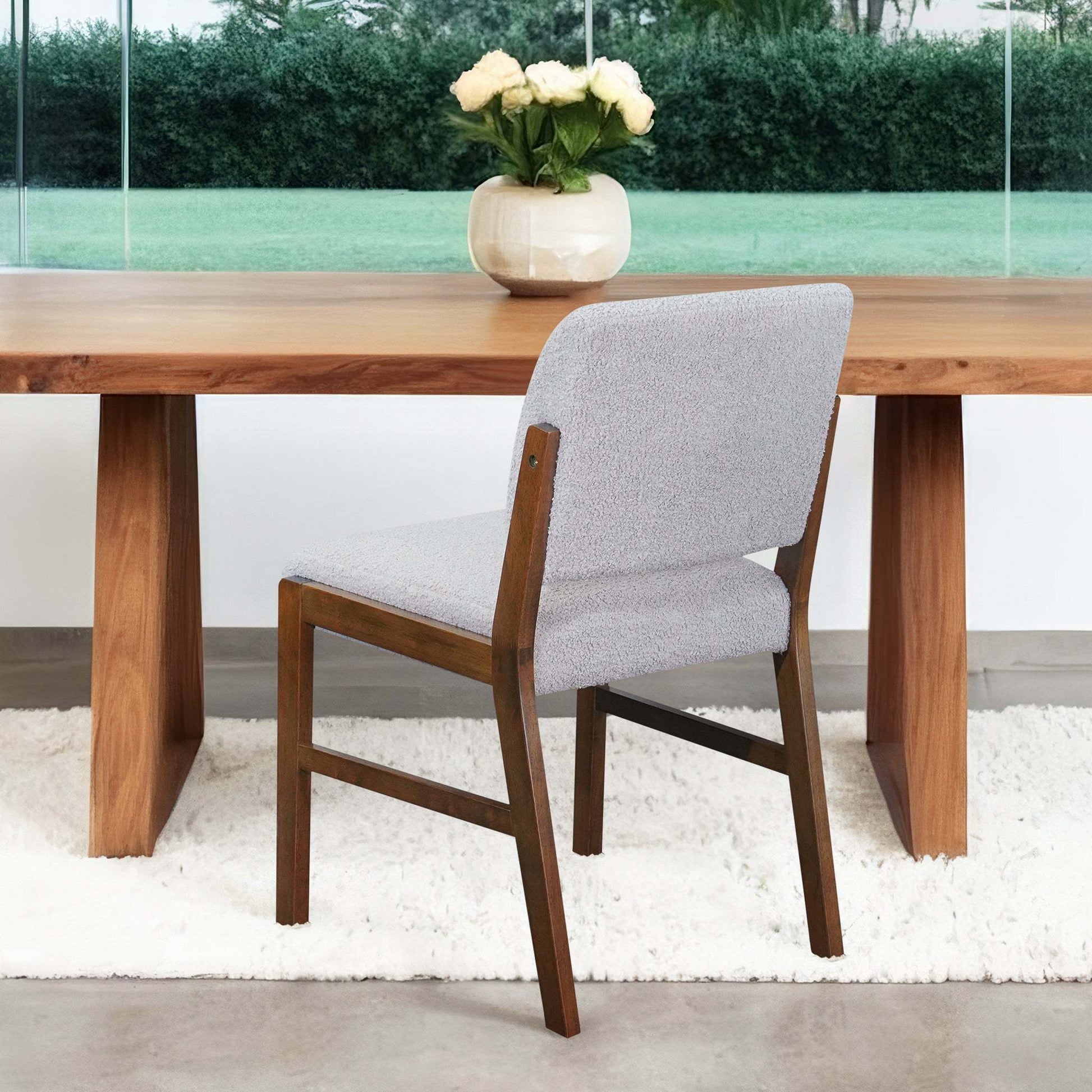 Modern wooden dining table with light gray upholstered chair and vase of white roses
