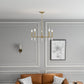 Modern living room with gold chandelier, tan sofa, geometric pillows, and gray paneled walls