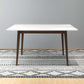 Modern dining table with white top and wooden legs on patterned rug, FredCo International furniture