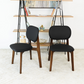 Modern black dining chairs with wood legs on cream carpet, bookshelf in background