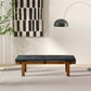 Modern black cushioned bench with wooden legs in stylish living room, abstract art on wall