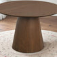 Round wooden dining table with conical base on patterned rug in modern home setting