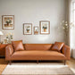 Modern brown leather sofa in bright living room with plant art, wood accents, and neutral rug