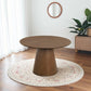 Modern round wooden dining table on patterned rug in bright living room with houseplant