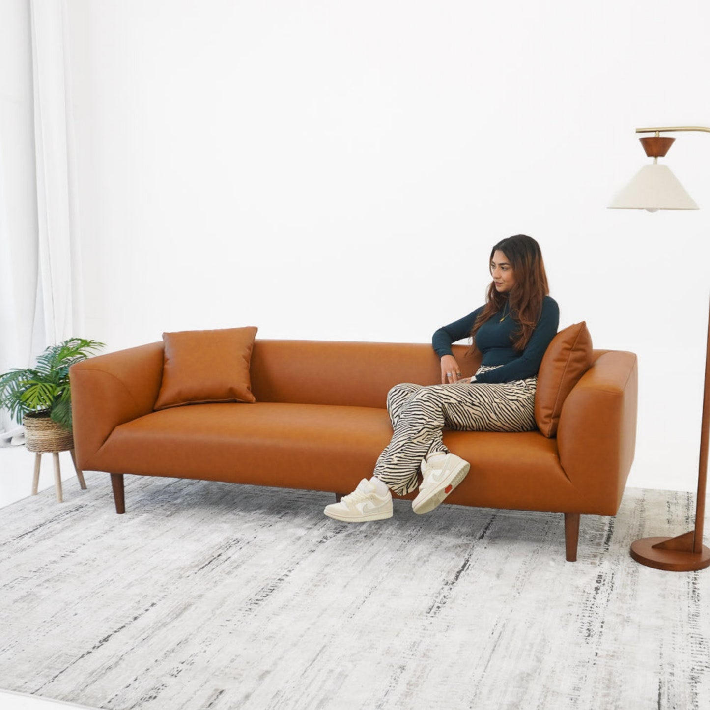 Modern tan leather sofa with two cushions, woman seated, in bright living room setting