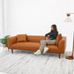 Modern tan leather sofa with two cushions, woman seated, in bright living room setting