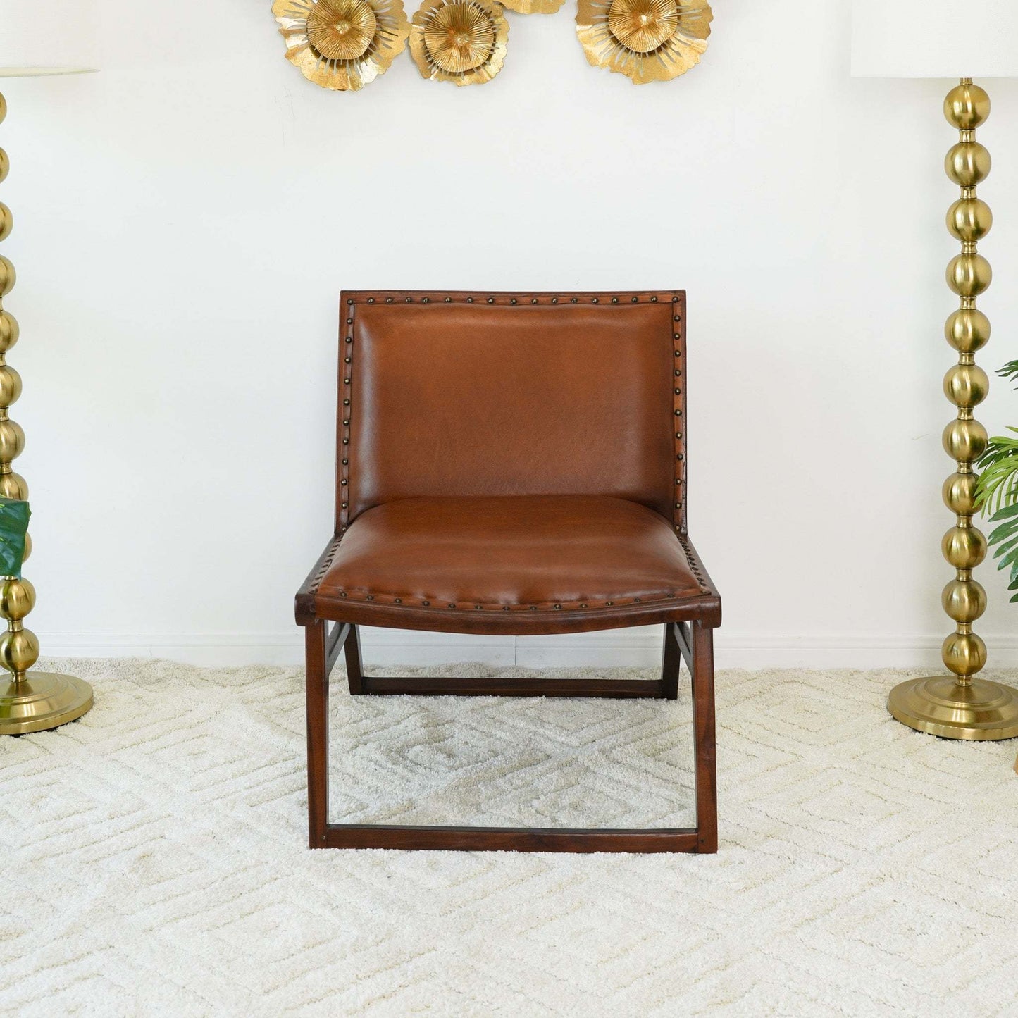 Brown leather accent chair with brass nailhead trim on beige rug, gold lamps and wall decor