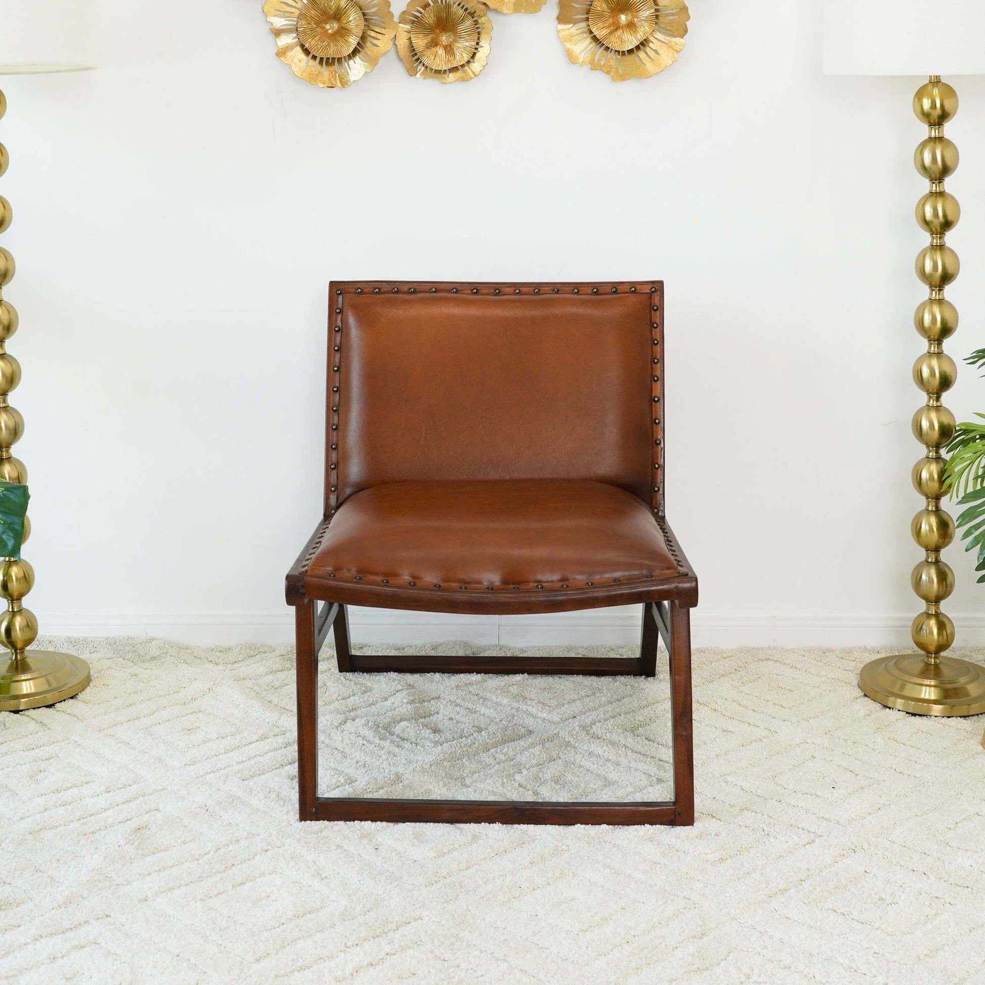 Brown leather accent chair with brass nailhead trim on beige rug, gold lamps and wall decor