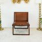 Brown leather accent chair with brass nailhead trim on beige rug, gold lamps and wall decor