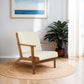 Mid-century modern wooden armchair with cream cushion on a round rug, potted plant, wall art