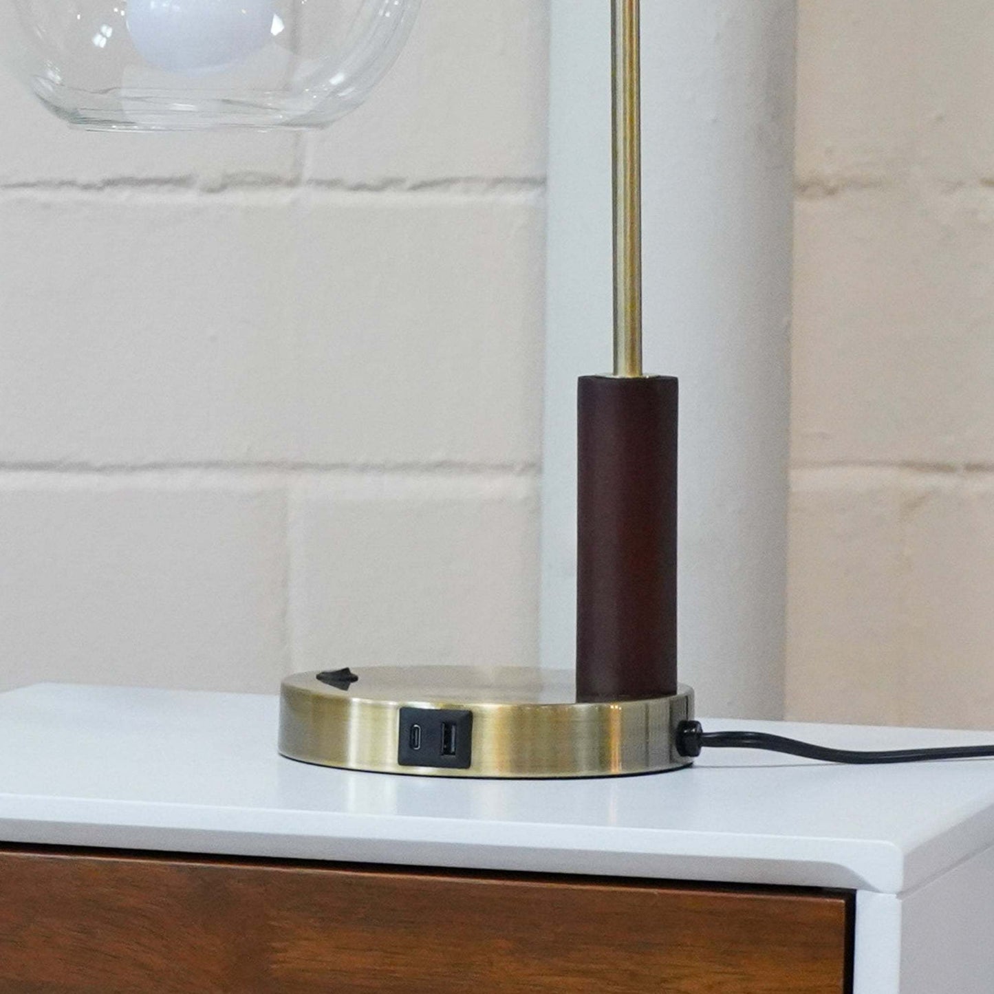 Modern table lamp with USB port on brass base, placed on white wood nightstand