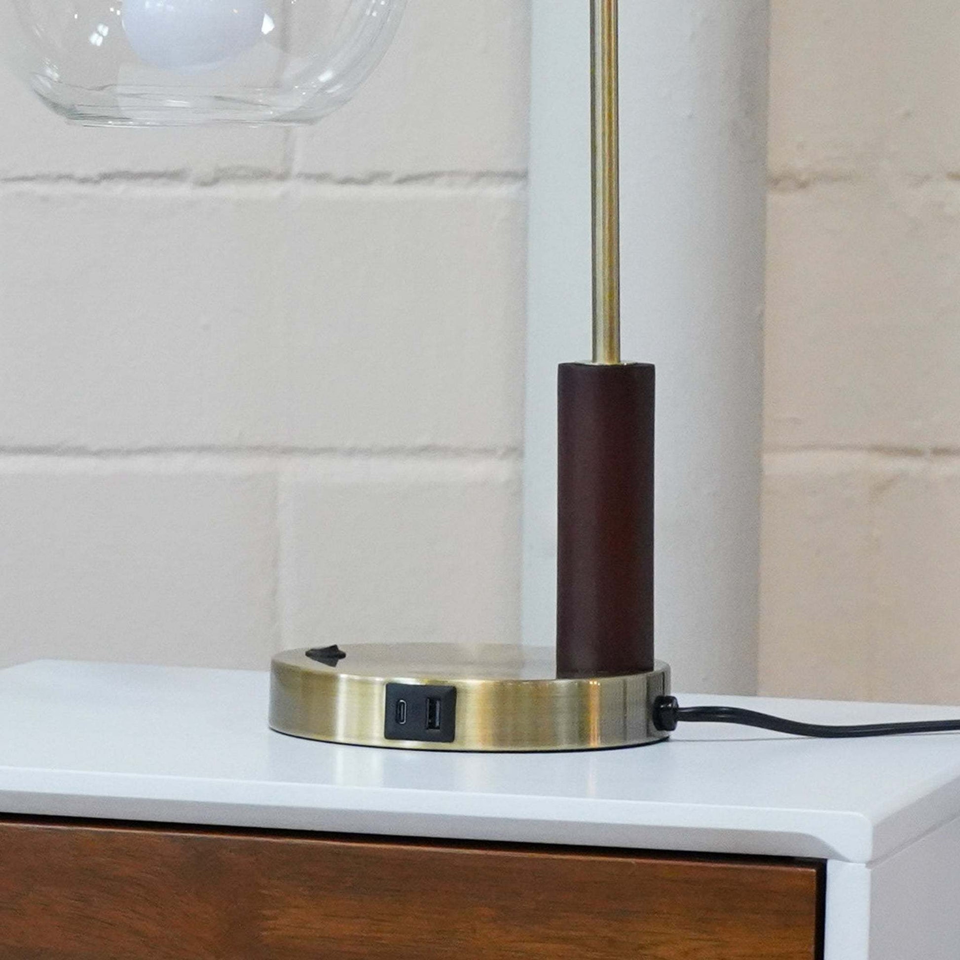 Modern table lamp with USB port on brass base, placed on white wood nightstand