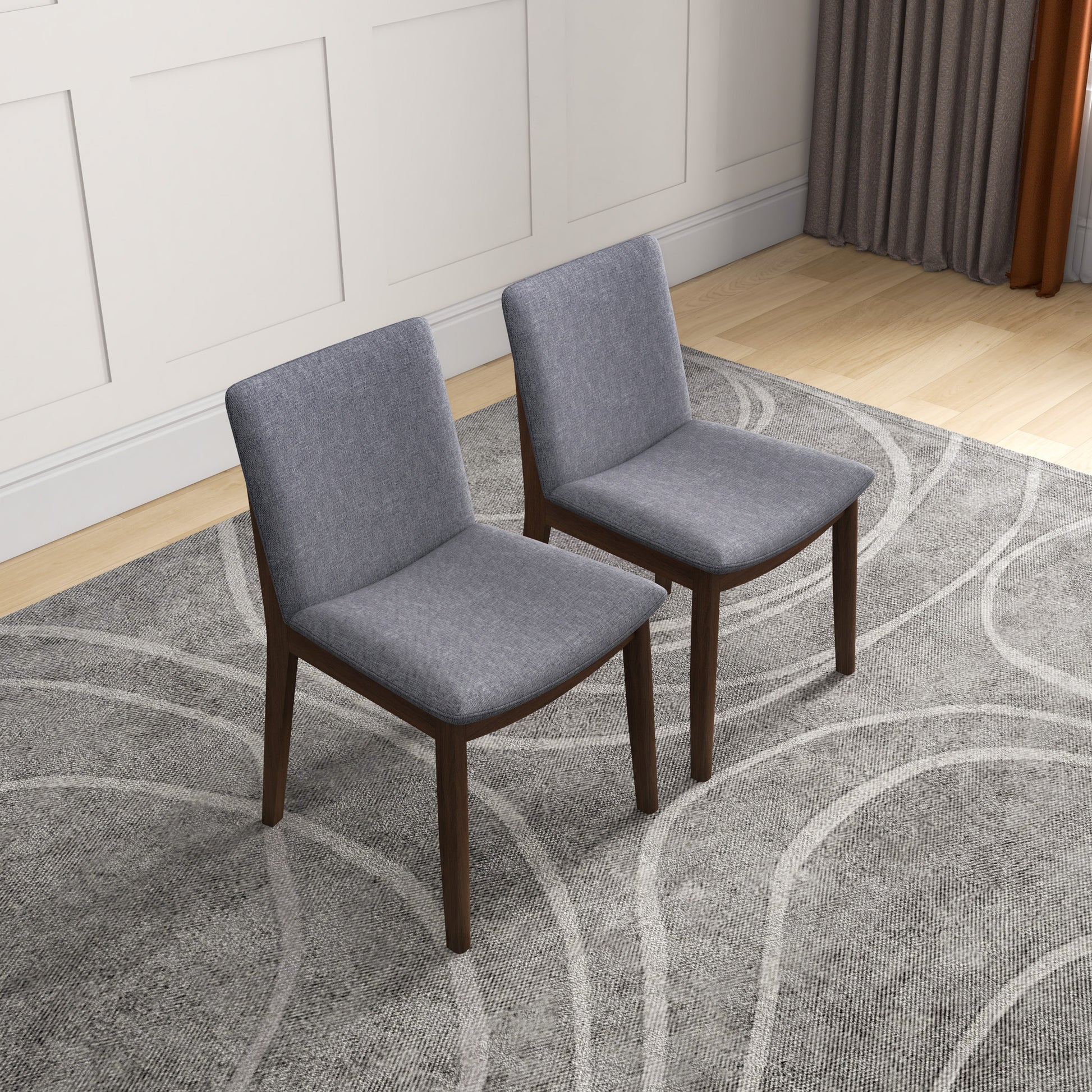 Two modern gray upholstered dining chairs with wooden legs on patterned rug in home setting