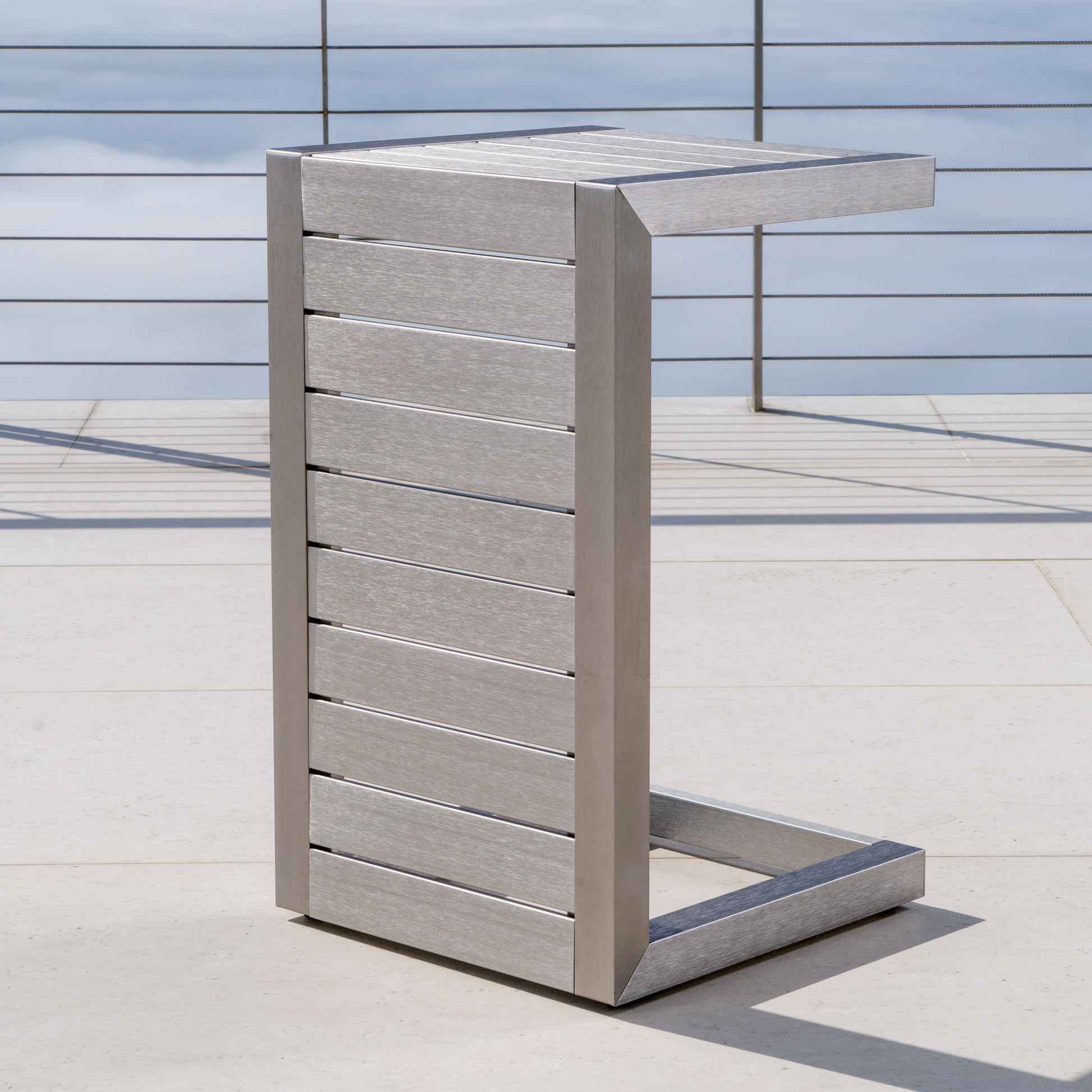 Modern stainless steel C-shaped side table on a patio, outdoor furniture by FredCo International
