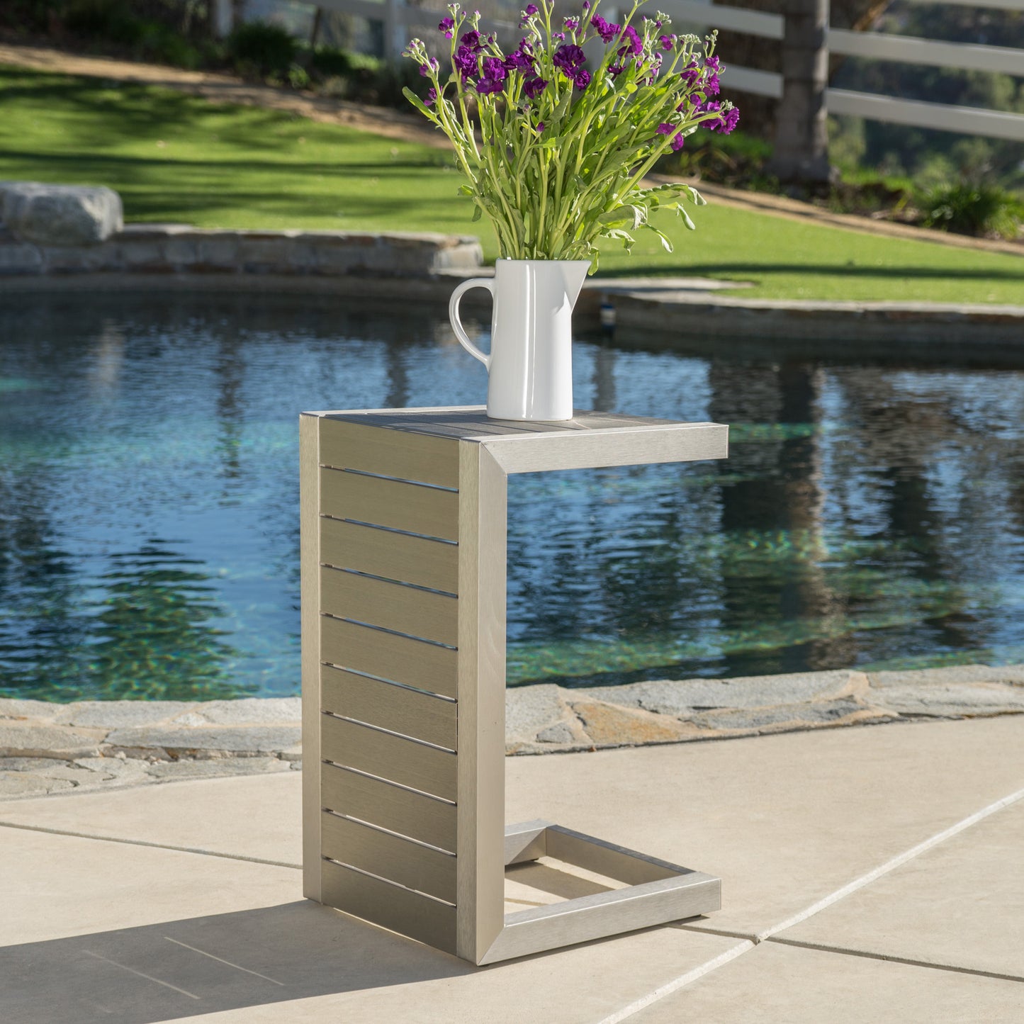 Modern metal outdoor side table with vase of purple flowers by a pool, FredCo International furniture