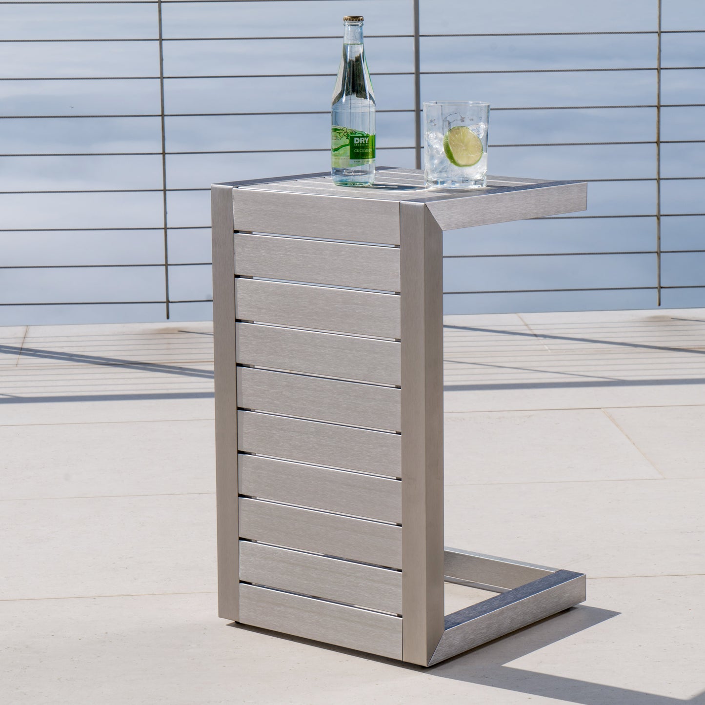 Modern patio side table with metal slats, glass of water and bottle, outdoor setting