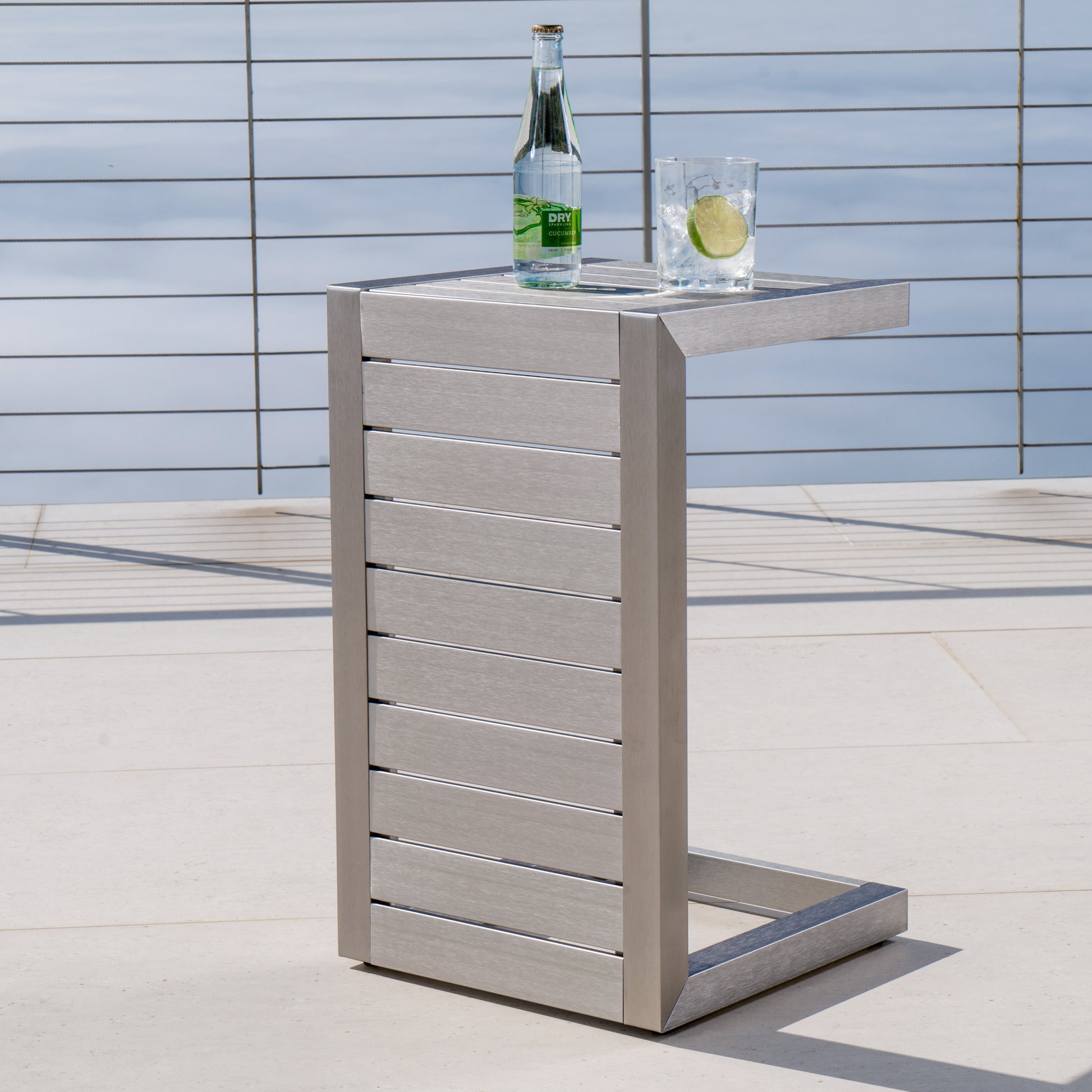 Modern patio side table with metal slats, glass of water and bottle, outdoor setting