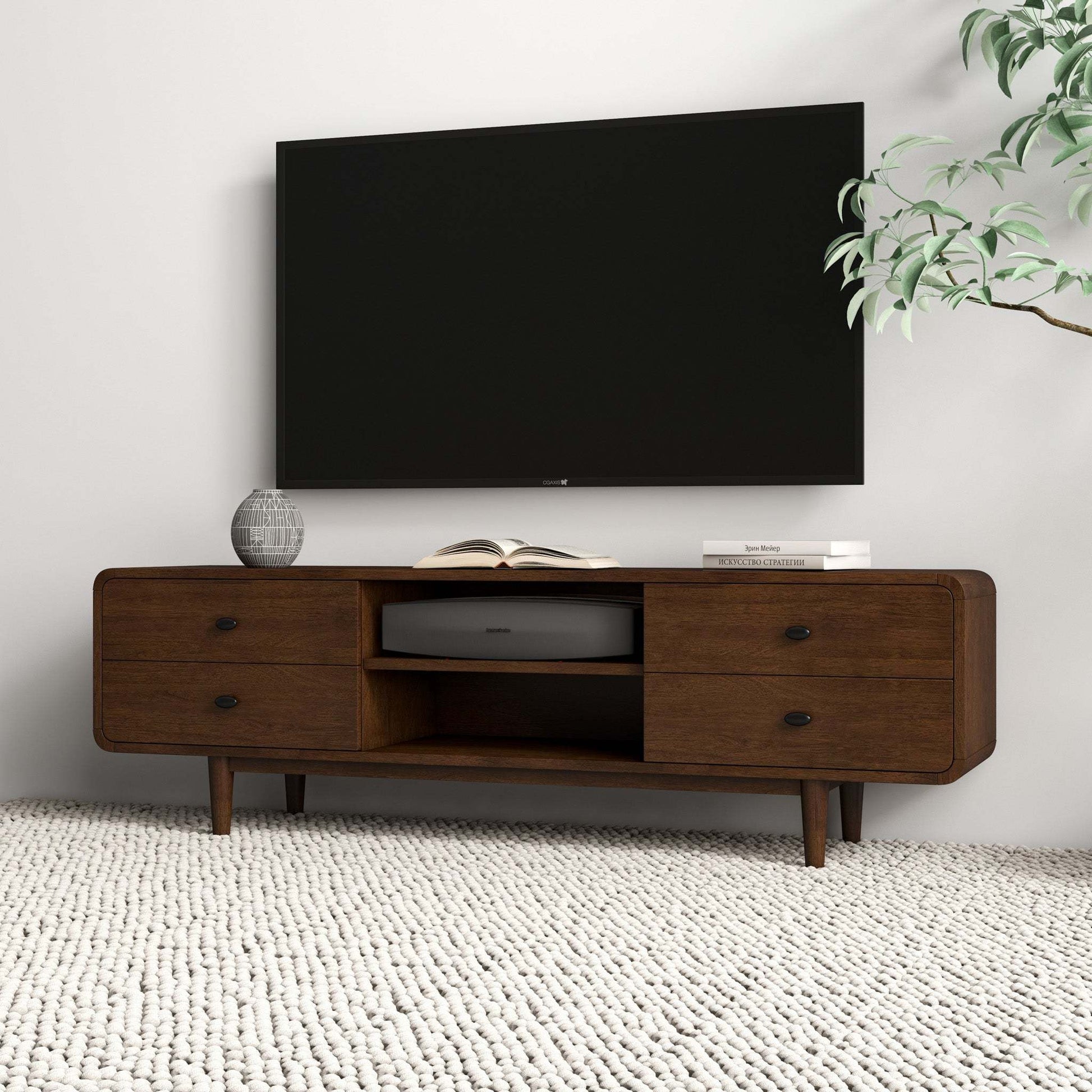 Modern wooden TV stand with drawers under wall-mounted television, vase, and books on top