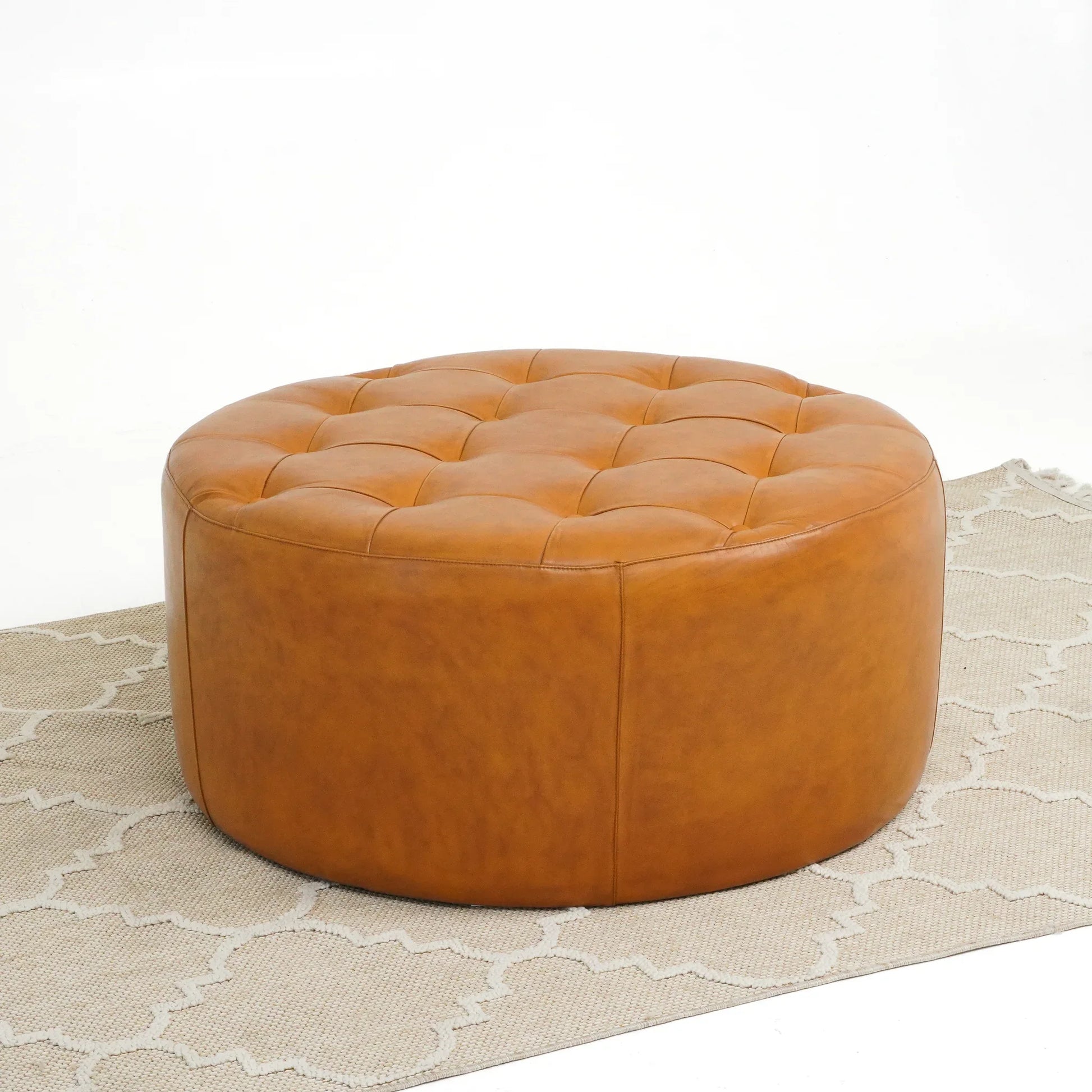 Round tufted leather ottoman on a beige patterned rug, modern furniture from FredCo International