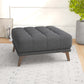 Modern dark gray tufted ottoman with wooden legs in a bright living room, FredCo International furniture