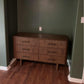 Mid-century modern wood dresser with vertical grooves, set against a green wall on hardwood floor.