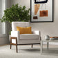 Modern living room with a beige armchair, yellow pillow, potted plant, and abstract wall art.