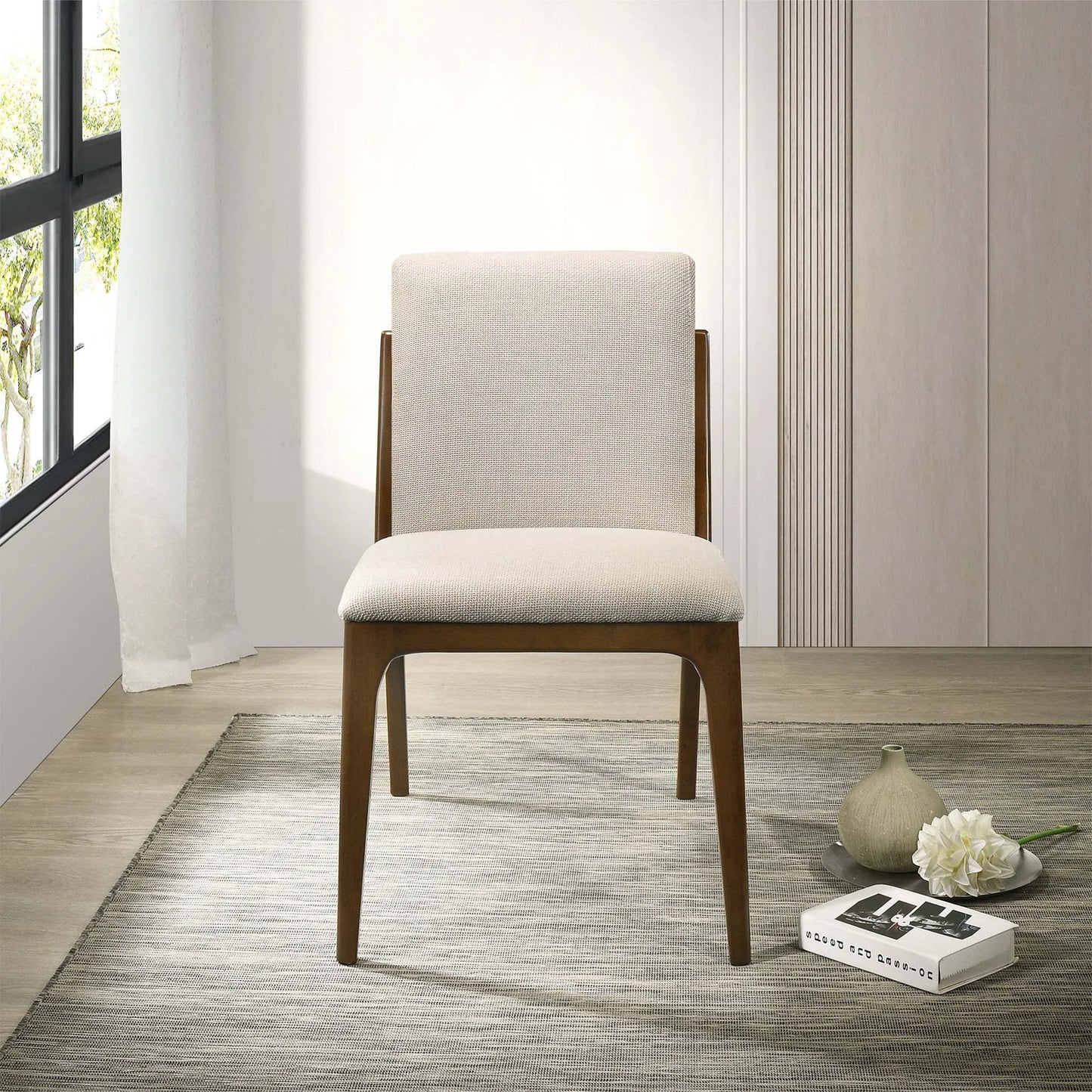 Modern beige upholstered dining chair with wooden frame on a rug, near a window and decor.