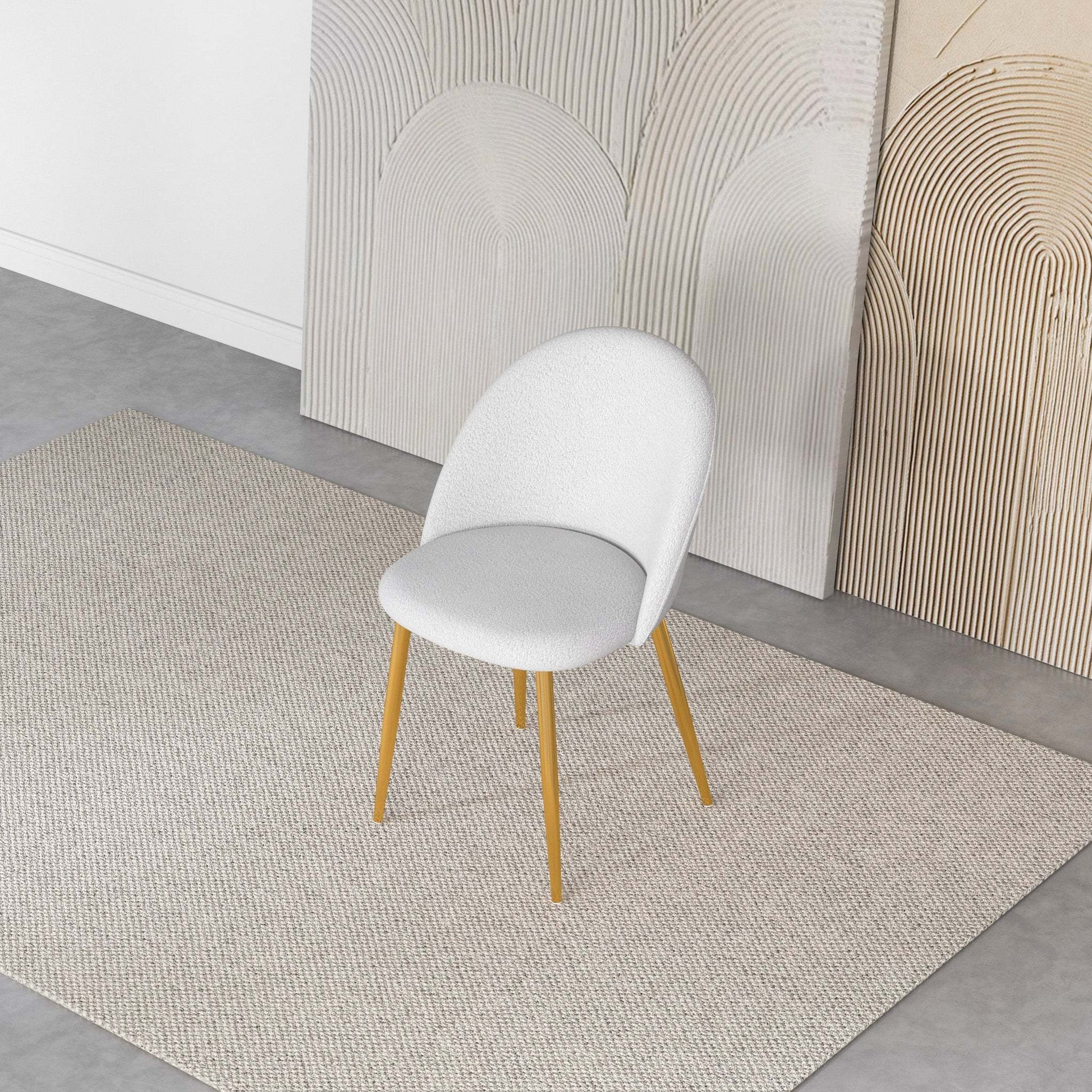 Modern white upholstered accent chair with gold legs on textured rug in contemporary room
