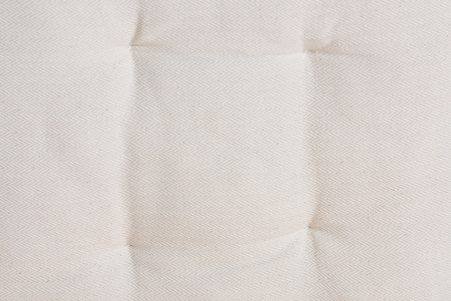 Close-up of cream-colored tufted mattress fabric with subtle herringbone pattern
