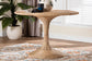 Round wicker dining table with flared base on patterned rug in bright living room
