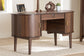 Mid-century modern wood desk with gold handles and decor, on beige rug in bright room