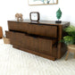 Mid-century modern wood dresser with open drawers, decor accents, and houseplant on beige rug