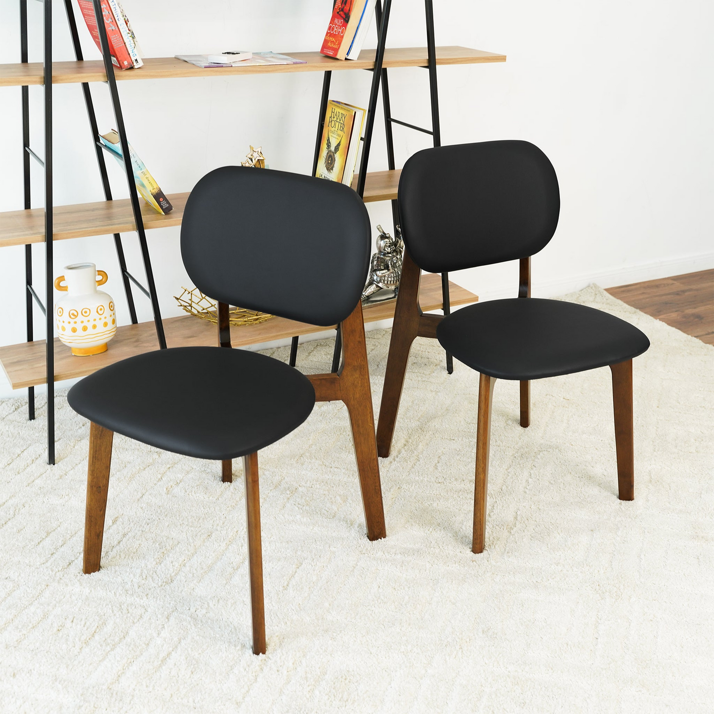 Set of two modern black and wood dining chairs on cream rug, bookshelf in background
