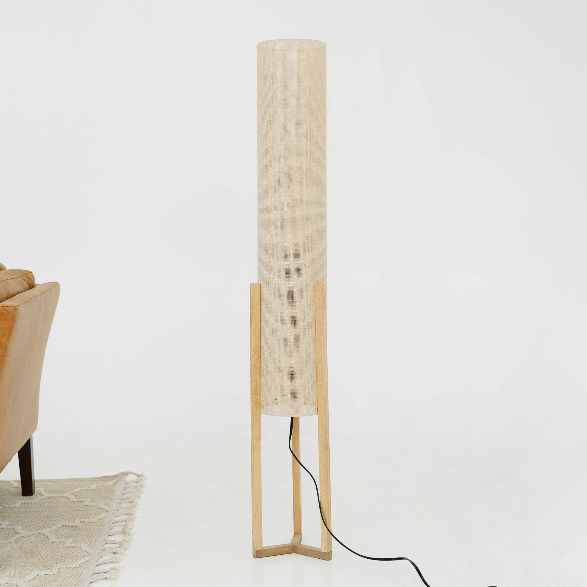 Modern floor lamp with beige fabric shade and wooden base beside tan sofa and patterned rug