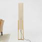 Modern floor lamp with beige fabric shade and wooden base beside tan sofa and patterned rug