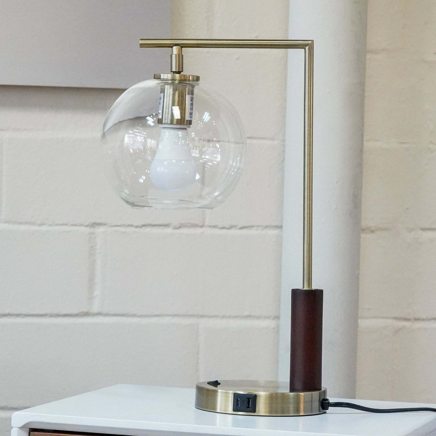 Modern table lamp with glass globe shade and brass finish on white nightstand, FredCo International furniture