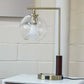 Modern table lamp with glass globe shade and brass finish on white nightstand, FredCo International furniture