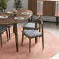 Modern wood dining table set with gray chairs on a pink rug, styled for FredCo International