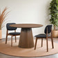 Modern round wooden dining table with two black cushioned chairs in a stylish home setting