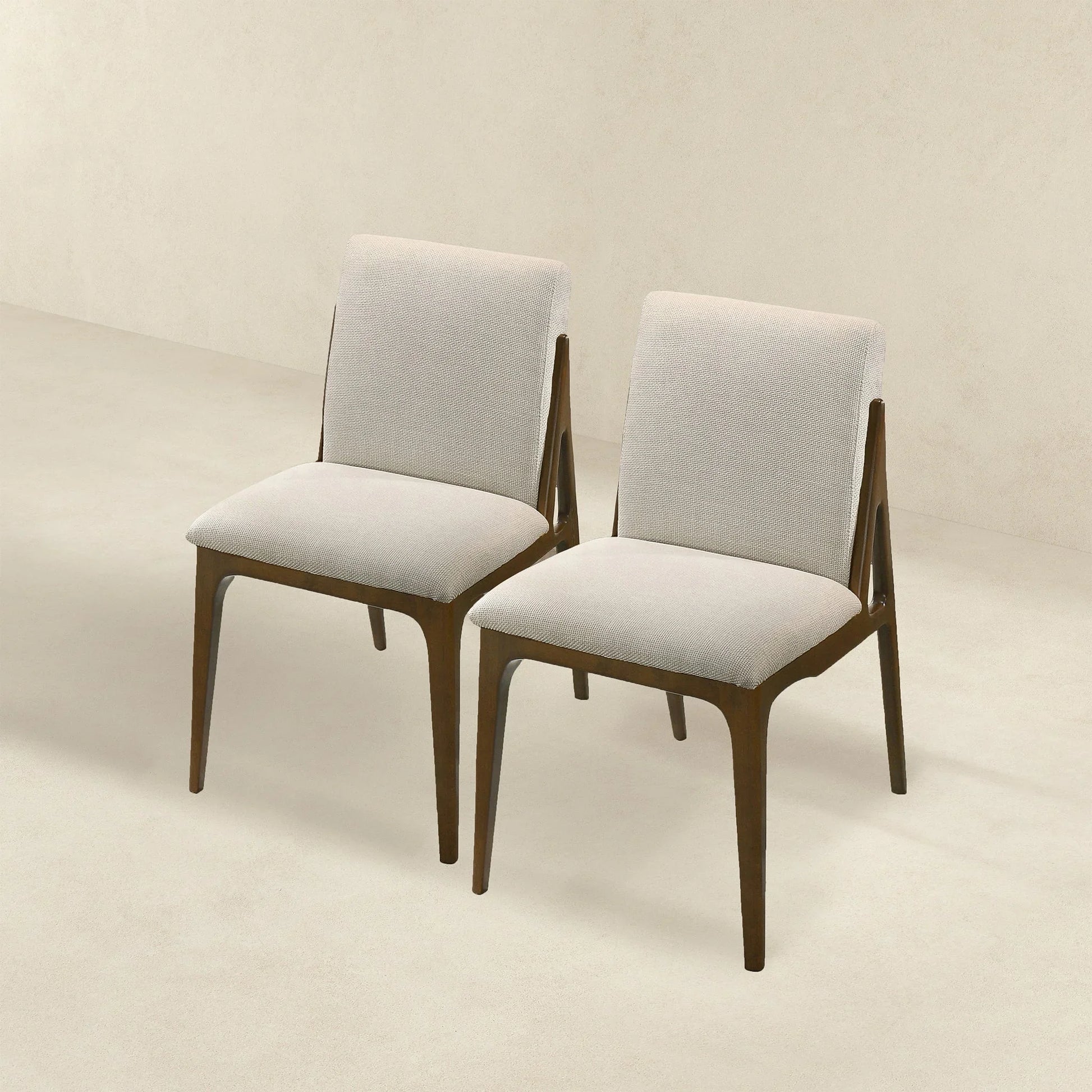 Pair of modern beige upholstered dining chairs with wooden legs on a neutral background