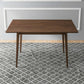 Modern wooden dining table on patterned gray rug in minimalist home setting