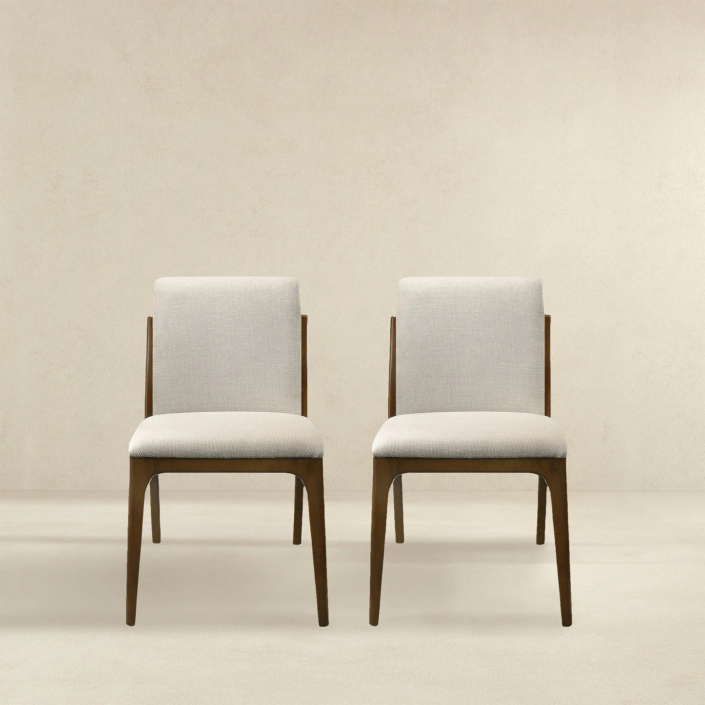 Pair of modern beige upholstered dining chairs with wooden legs on neutral background