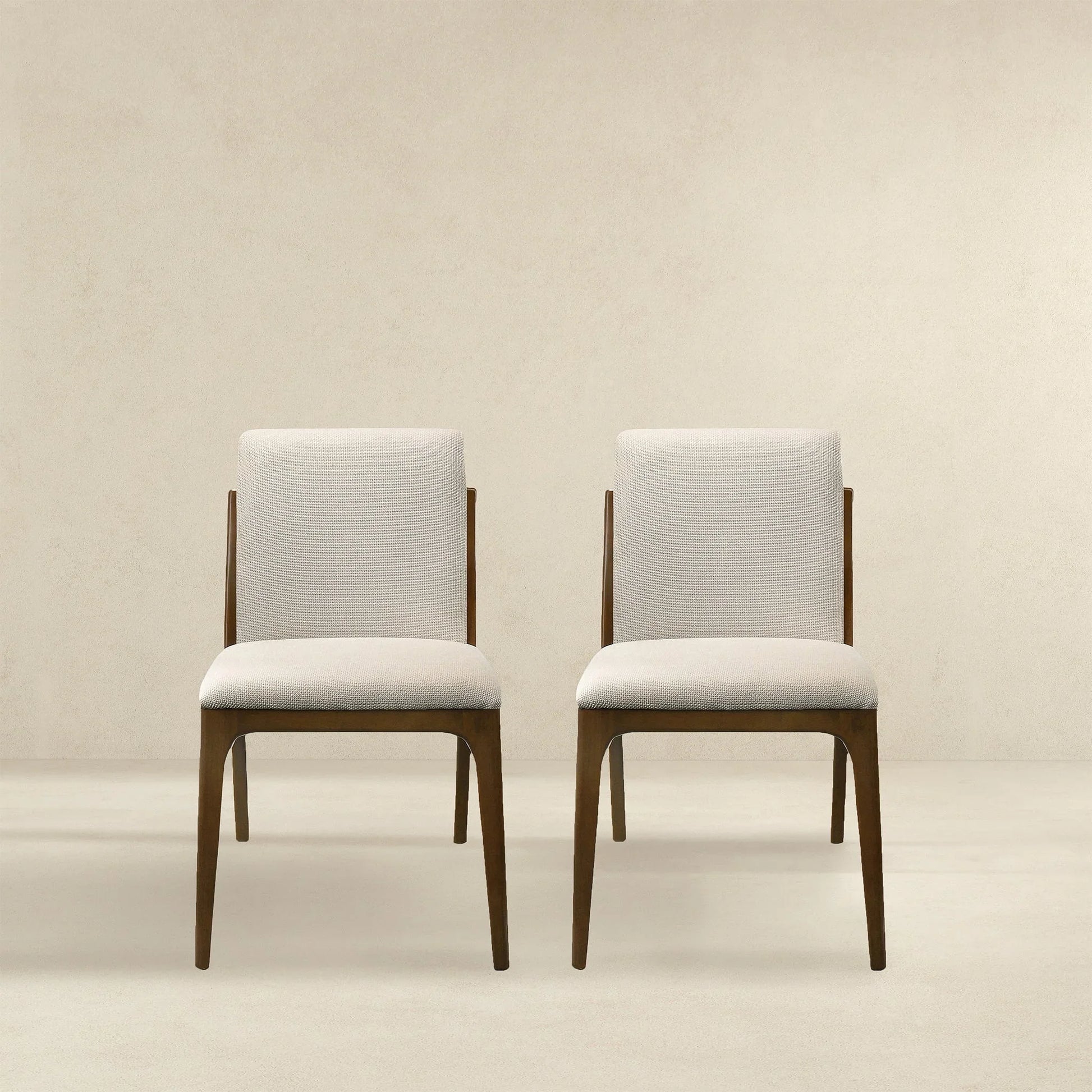 Pair of modern beige upholstered dining chairs with wooden legs on neutral background