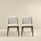 Pair of modern beige upholstered dining chairs with wooden legs on neutral background