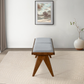 Modern wooden bench with gray cushion on patterned rug, with framed wall art and potted plant